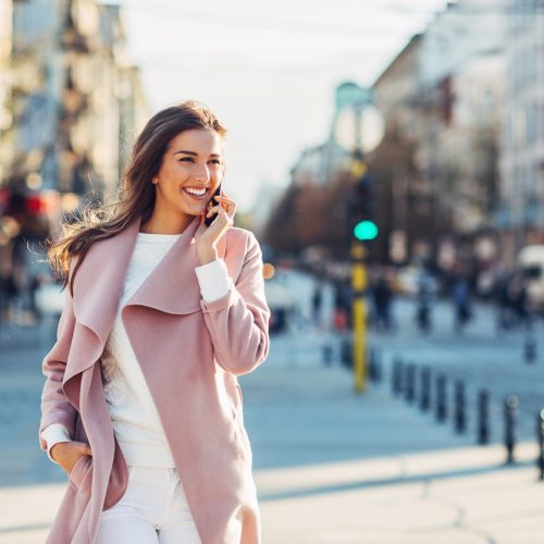 Elegant woman walking on the sidewalk at urban setting and talking on the phone, with copy space.